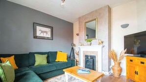 Una sala de estar con un sofá verde, una chimenea, un televisor y un espejo en la pared.