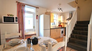 A compact kitchen with a microwave, refrigerator, and a dining area with a table set for two. - Sea Whisper- lovely home in charming village (Pittenweem)