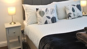 A neatly arranged bedroom with a bed, two bedside tables, a nightstand, a wall-mounted painting, and a lamp. - Sea Whisper- lovely home in charming village (Pittenweem)