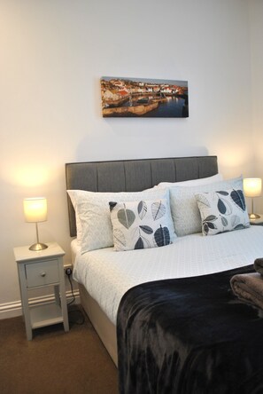 A neatly arranged bedroom with a bed, two bedside tables, a nightstand, a wall-mounted painting, and a lamp. - Sea Whisper- lovely home in charming village (Pittenweem)