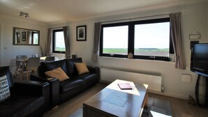 Ein Wohnzimmer mit einer schwarzen Ledersofa, einem Holztisch und einem großen Fenster mit Blick auf die Landschaft.
