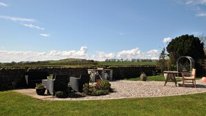 Ein Garten-Terrasse mit Gartenmöbeln, einer Steinmauer und Blick ins Grüne.