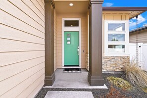 Une maison avec une porte verte, un revêtement de couleur beige et un mur d’accent en pierre.