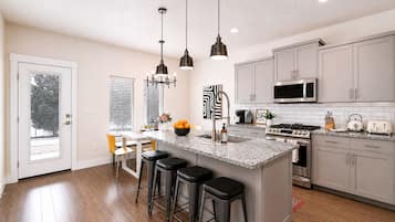 A modern kitchen with a central island, bar stools, stainless steel appliances, and pendant lighting.