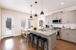 A modern kitchen with a central island, bar stools, stainless steel appliances, and pendant lighting. - Top Rated • Luxe • Spotless • Quiet • Prime Area by The Village at Meridian (Meridian)