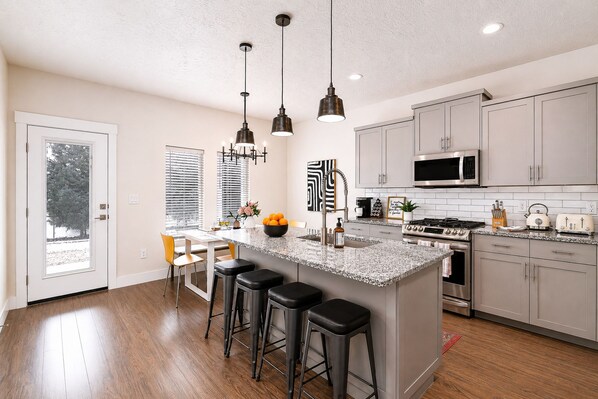 A modern kitchen with a central island, bar stools, stainless steel appliances, and pendant lighting.