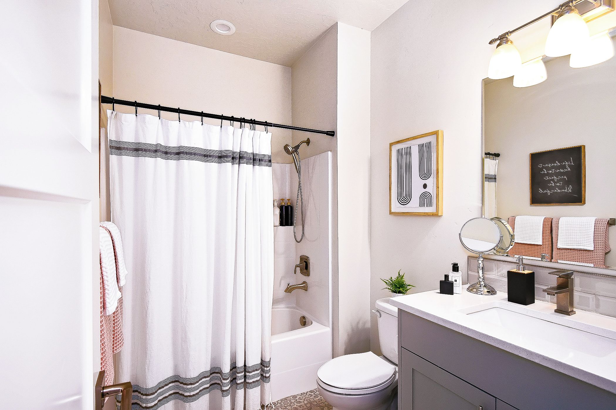 Une salle de bain équipée d’un rideau de douche, d’une baignoire, de toilettes, d’un lavabo avec un miroir et d’un porte-serviettes.