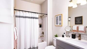Une salle de bain équipée d’un rideau de douche, d’une baignoire, de toilettes, d’un lavabo avec un miroir et d’un porte-serviettes.