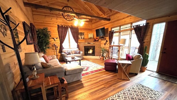 A cozy log cabin interior with a fireplace, wooden furniture, and a large window.