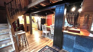 A rustic interior with a wooden staircase, a dining area with white chairs, and a kitchen with wooden cabinets.