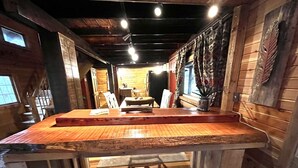 A wooden interior with a central table and chairs, a staircase, and a window.