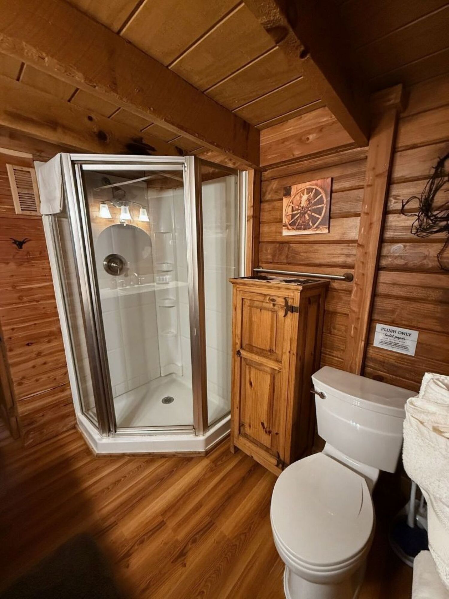 Un baño de cabaña de madera con ducha envuelta en vidrio, un armario de madera y un inodoro.