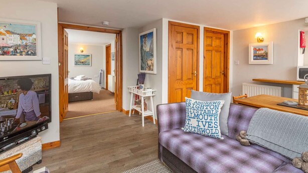 A cozy living room with a sofa, a television, and a dining area. There are wooden doors and a hallway leading to another room. - East Pier View- stunning shorefront home (Saint Monans)