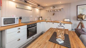 A compact kitchen with a microwave, stove, and sink. There is a wooden table with a mat and a decorative item. - East Pier View- stunning shorefront home (Saint Monans)