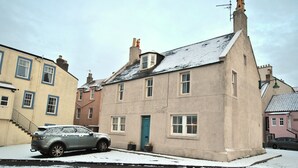 A residential building with a snow-covered street, a parked car, and a visible front door. - East Pier View- stunning shorefront home (Saint Monans)