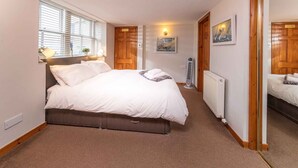 A bedroom with a large bed, a radiator, wooden doors, and a small window. - East Pier View- stunning shorefront home (Saint Monans)