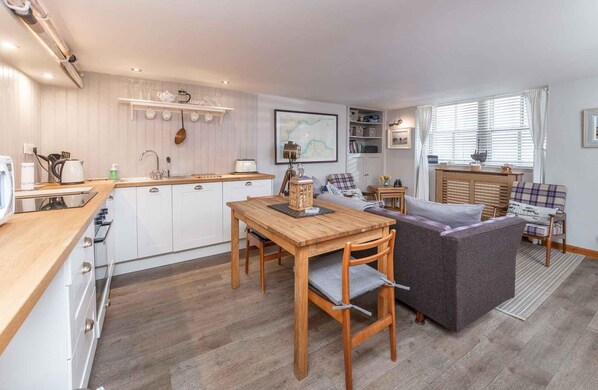 Un espacio habitable compacto con kitchenette, comedor y zona de estar con sofá y una mesita.