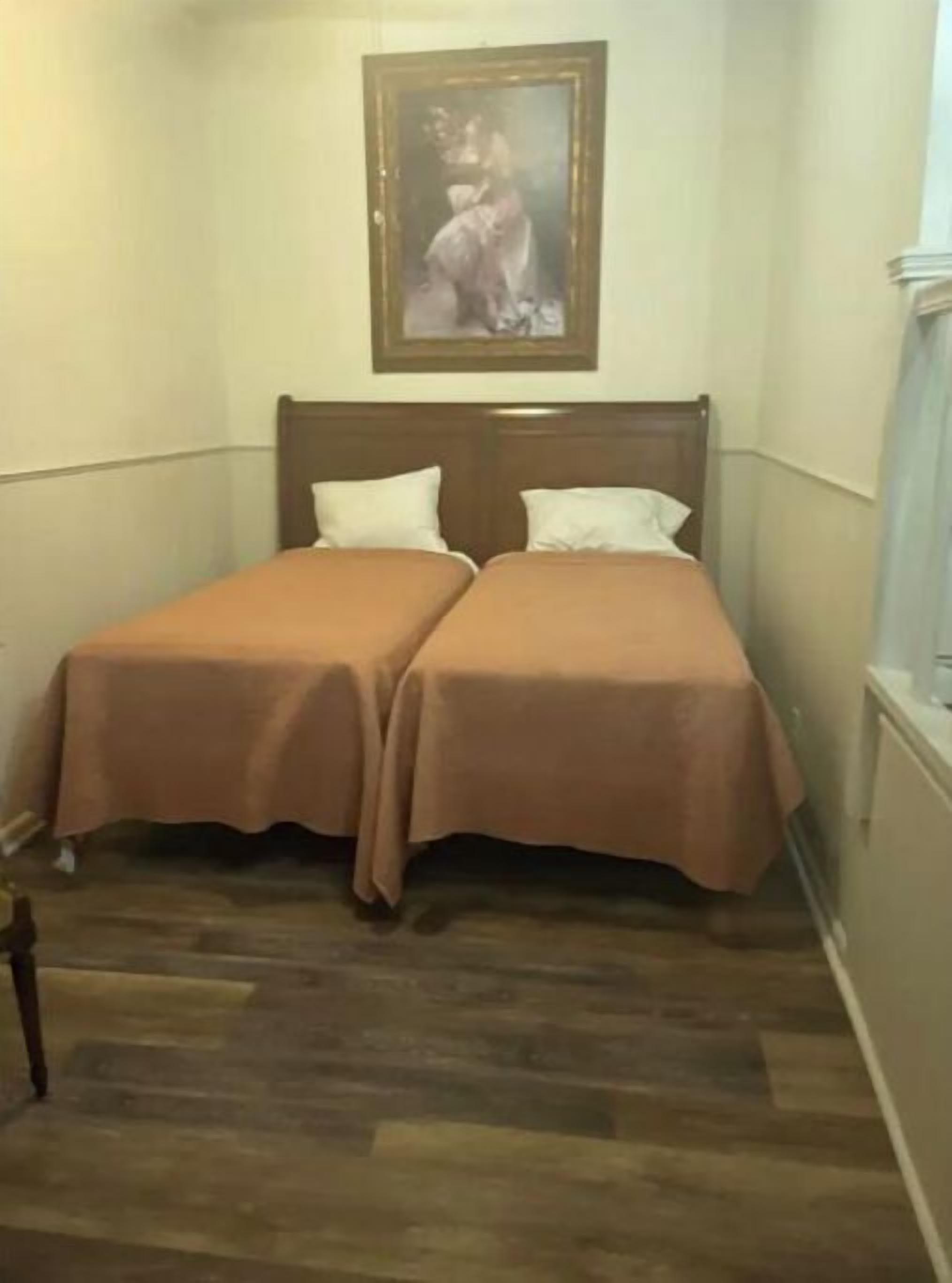 A room with two beds, a wooden headboard, a framed picture on the wall, and a wooden floor.