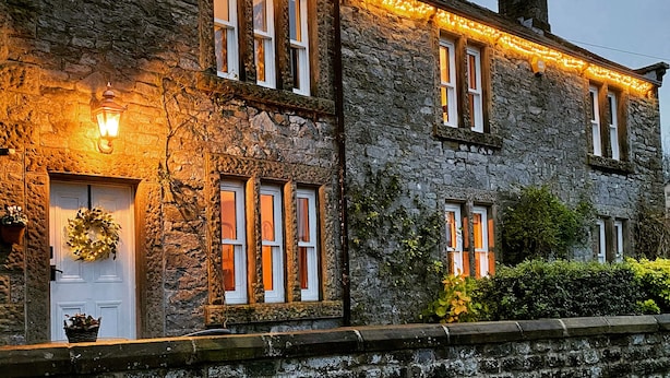 Un bâtiment en pierre doté de nombreuses fenêtres, une porte ornée d’une guirlande et illuminée de guirlandes lumineuses.
