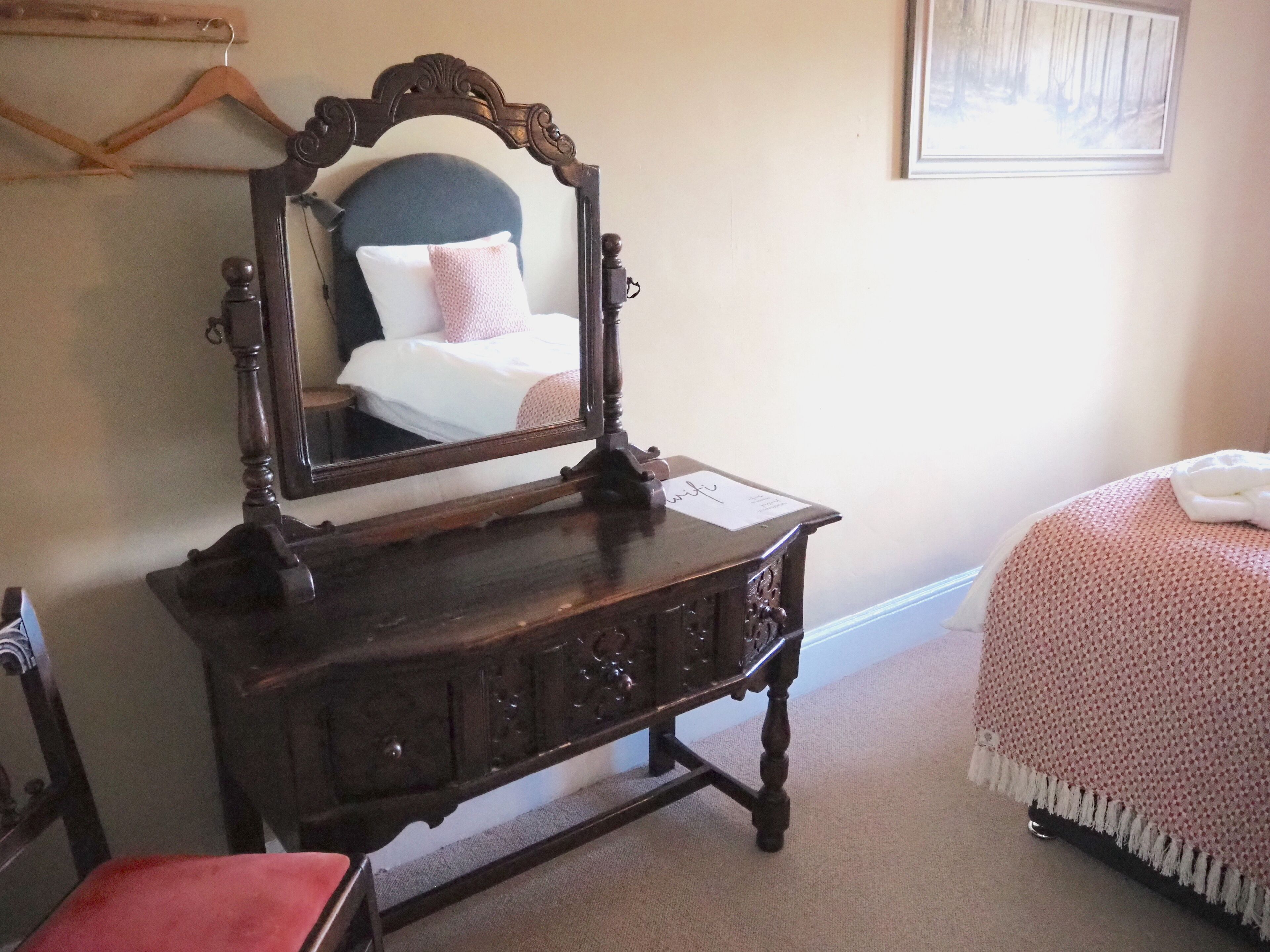Un aparador de madera con espejo, una cama con una colcha rosa y un cuadro enmarcado en la pared.