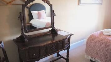 Un aparador de madera con espejo, una cama con una colcha rosa y un cuadro enmarcado en la pared.