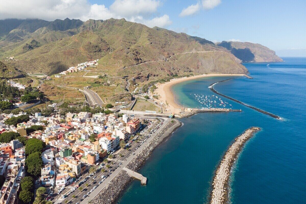 Vista aérea de un pueblo costero con una playa, una carretera que lleva a la playa y edificios a lo largo de la costa.