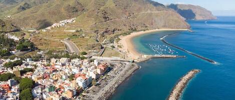 Vista aérea de un pueblo costero con una playa, una carretera que lleva a la playa y edificios a lo largo de la costa.