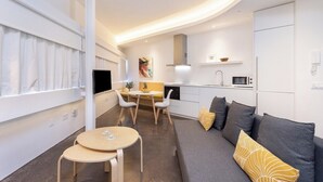 A modern, compact living space with a sofa, a dining table, and a kitchen area.