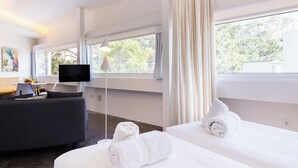 Una habitación de hotel moderna con una cama, un sofá, un televisor y ventanas amplias.