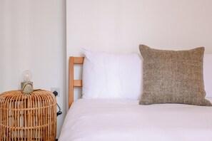 A bed with white bedding, a wooden headboard, and a textured pillow. - Stylish 2BD Victorian Home near Holland Park (London)