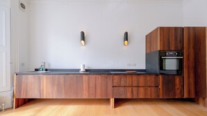 A modern kitchen with a wooden countertop, two wall-mounted lights, a built-in oven, and a wooden cabinet. - Stylish 2BD Victorian Home near Holland Park (London)