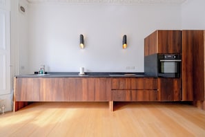 A modern kitchen with a wooden countertop, two wall-mounted lights, a built-in oven, and a wooden cabinet. - Stylish 2BD Victorian Home near Holland Park (London)