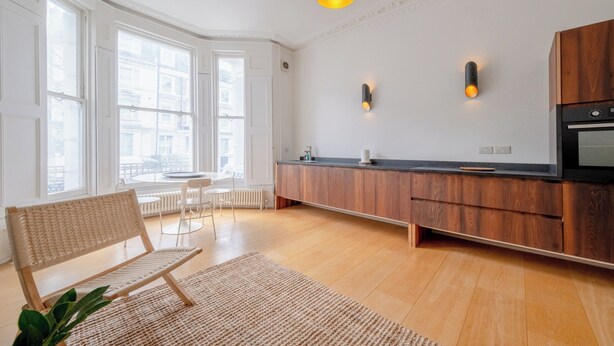 A modern kitchen with wooden cabinets, a black countertop, and a built-in oven. - Stylish 2BD Victorian Home near Holland Park (London)
