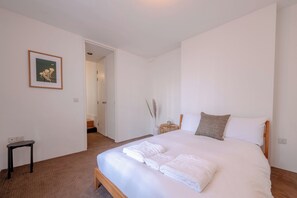 Un dormitorio con una cama, una mesita de noche, una silla y un cuadro en la pared.