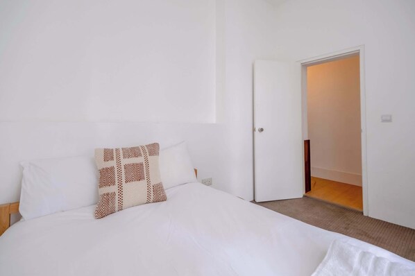 A hotel room with a bed, a door, and a light switch on the wall.