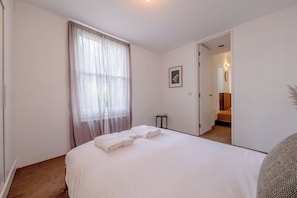 A hotel room with a bed, a window with curtains, a framed picture on the wall, and a door leading to a bathroom.