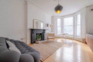 A modern living room with a fireplace, a sofa, a dining area, and large windows.