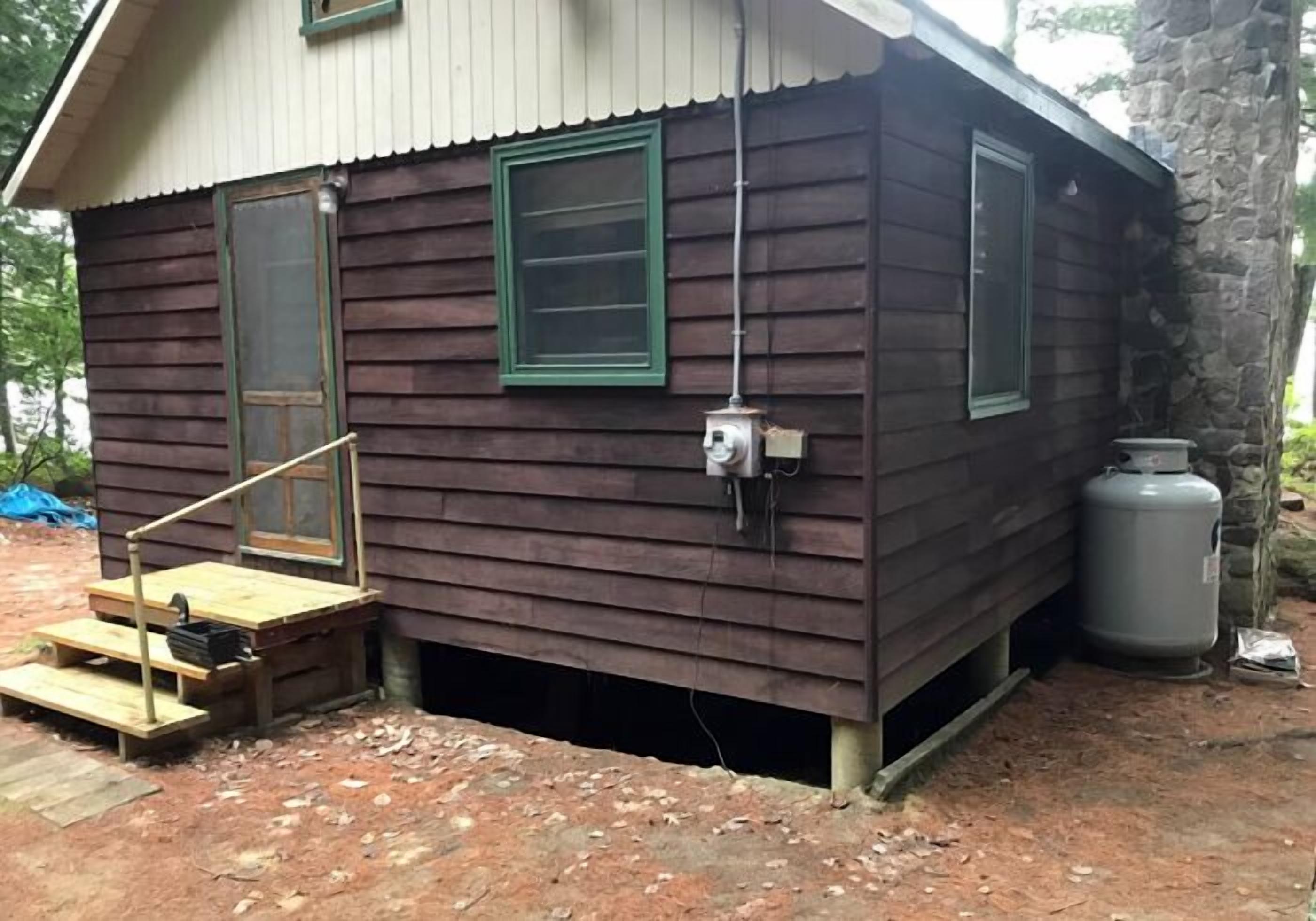 Une petite cabane en bois avec un toit en métal, une véranda en bois avec des marches et un coffret électrique fixé au mur.