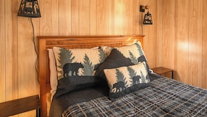 A wooden-paneled room with a bed, two wall-mounted lamps, and a small table.