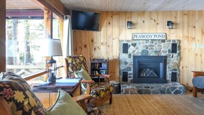 A cozy living room with a stone fireplace, wooden walls, a television mounted above it, and a sign reading "PEABODY POND".