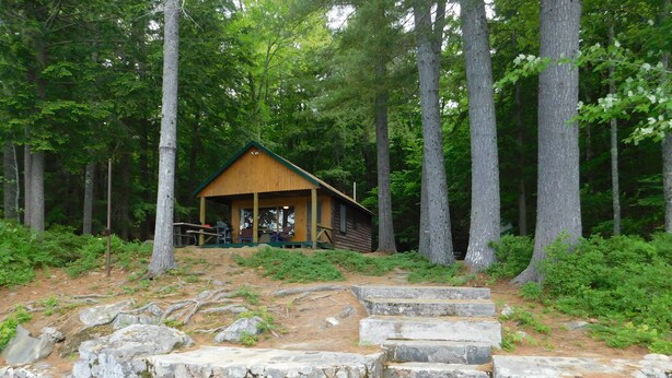 A rustic cabin with a wooden deck and stone steps leading to a wooden dock over water.