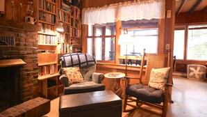 Een gezellige kamer met een open haard, een boekenkast, een comfortabele zithoek met een schommelstoel en een raam met uitzicht.