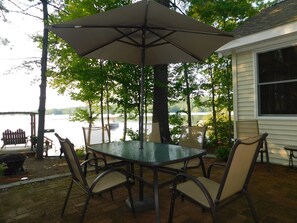 A patio with a glass table and chairs, an umbrella, and a view of a lake. - Charming pet-friendly waterfront home with beautiful views of Highland Lake! (Bridgton)