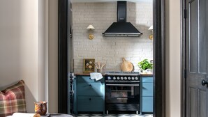 Una cocina con estufa negra, pared de ladrillo blanco y suelo a cuadros.