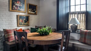 Un comedor con una mesa redonda de madera, sillas, una araña y una ventana con cortinas.