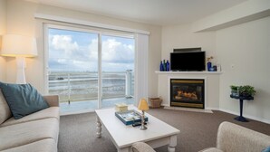 Ein Wohnzimmer mit einer Couch, einem Couchtisch, einem Kamin, einem Fernseher und Meerblick durch ein großes Fenster.