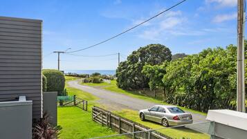 A residential street with a parked car, a wooden fence, and a view of the sea.