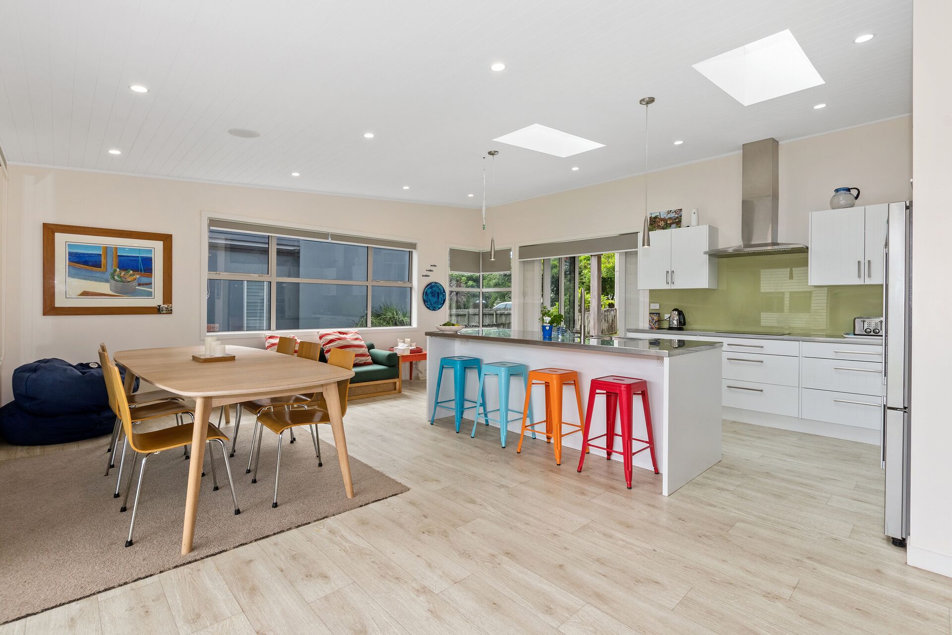 A modern kitchen with a dining area, large windows, and colorful stools.