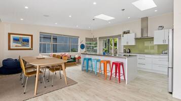 A modern kitchen with a dining area, large windows, and colorful stools.