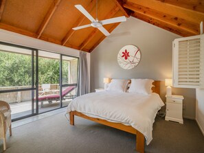 Un dormitorio con cama, ventilador de techo, mesita de noche y ventana con vista a la vegetación.